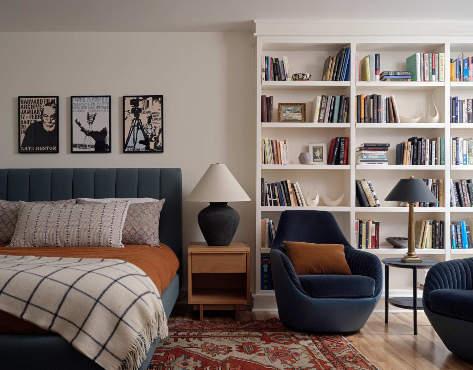 A basement bedroom with a bed, two chairs and a book shelf - Before Image