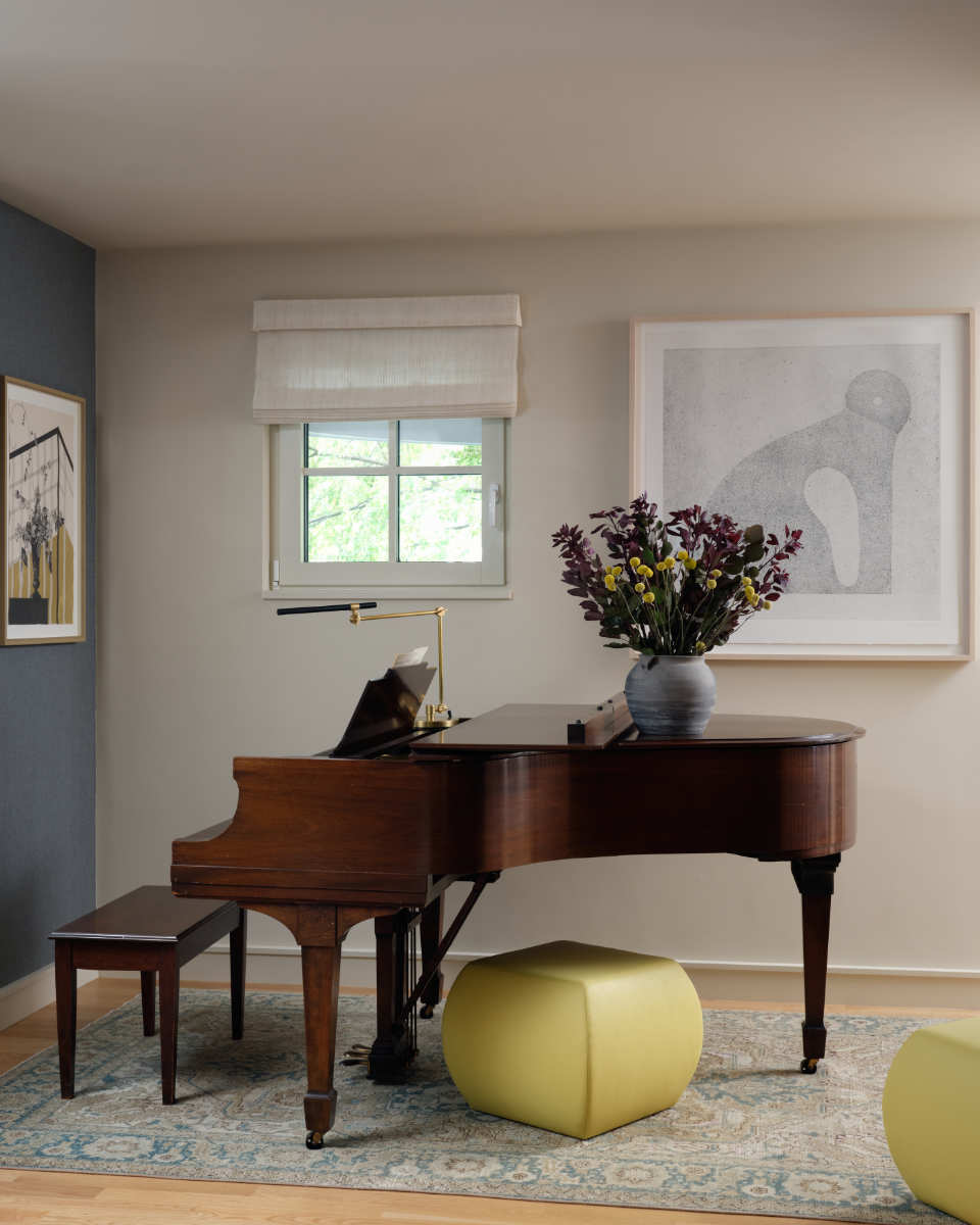 A living room with a piano and a vase of flowers - Before Image